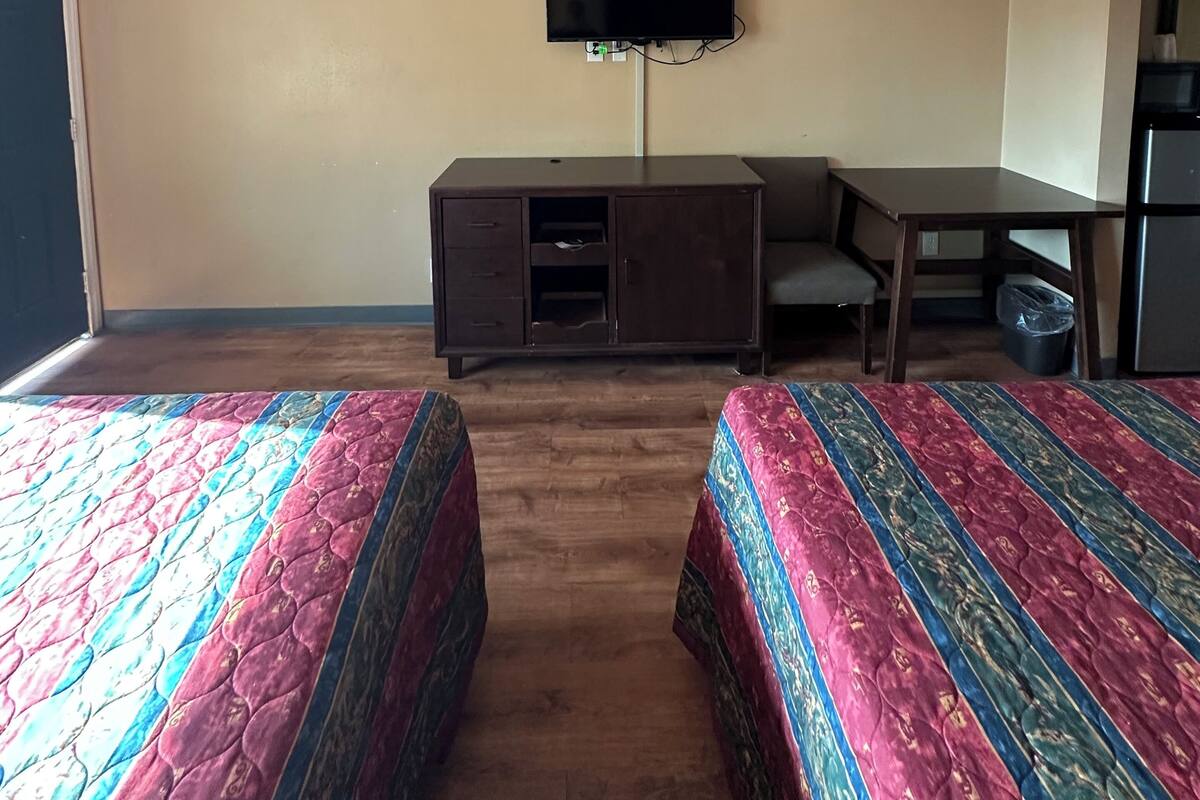 A hotel room with two beds, a desk, a television, and a refrigerator.