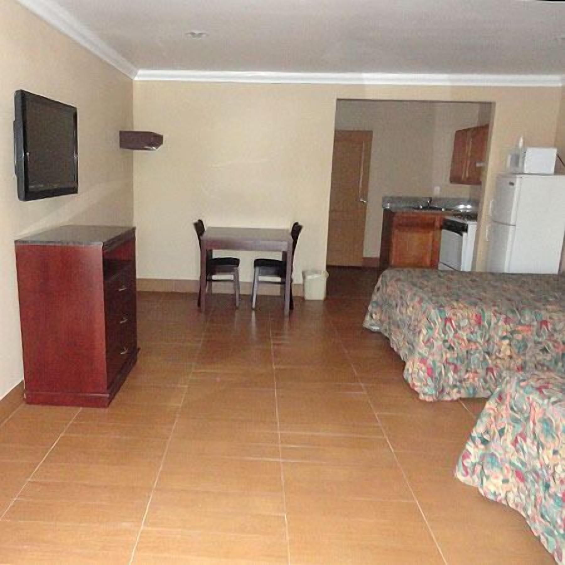 A hotel room with a bed, a desk, a chair, a television, and a kitchenette.