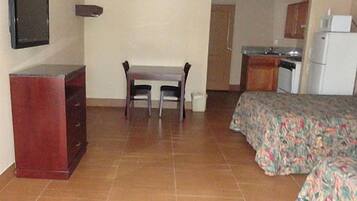 A hotel room with a bed, a desk, a chair, a television, and a kitchenette.