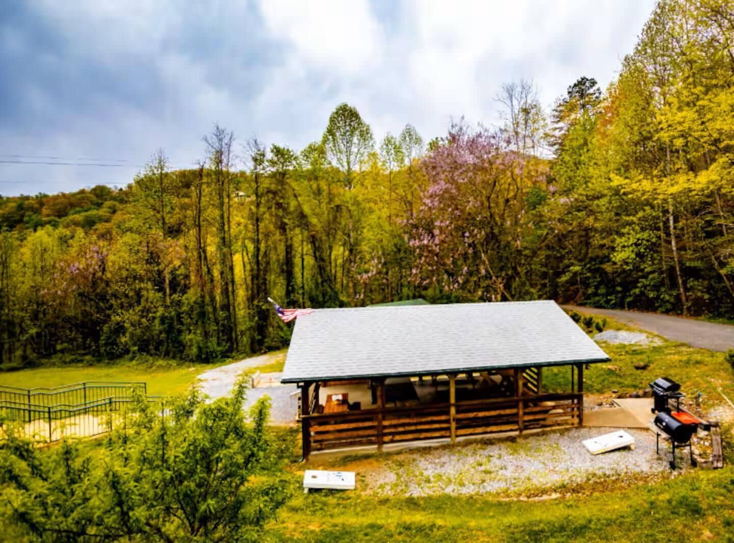 A rustic cabin with a metal roof and wooden walls, surrounded by a fenced yard and a gravel path.