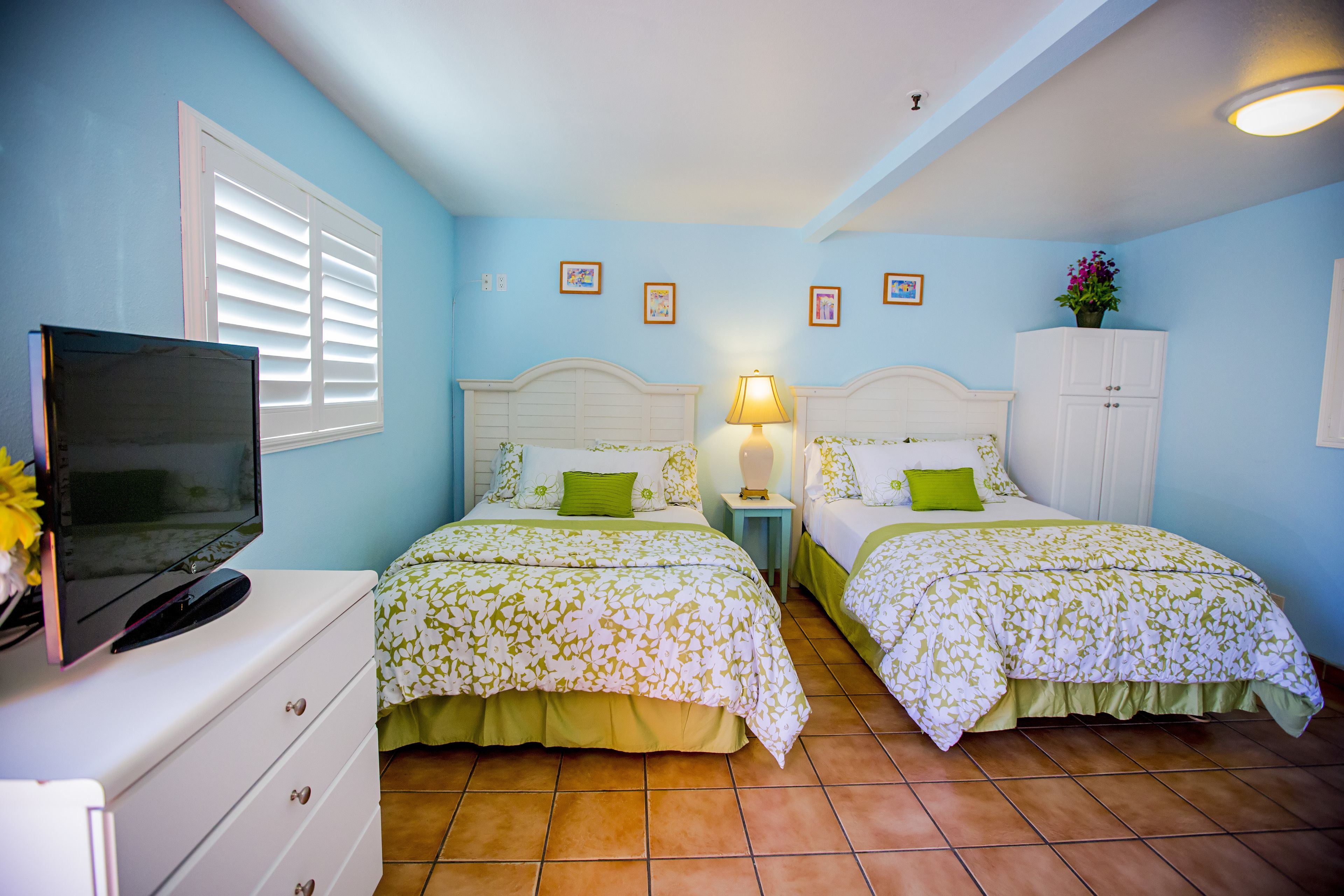 Un dormitorio con dos camas, un televisor sobre una cómoda y una mesita de noche con una lámpara.