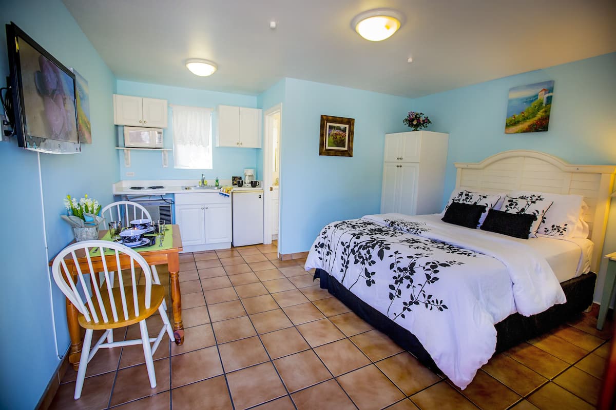 A bedroom with a bed, a desk with a chair, a microwave, and cabinets.
