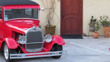 A vintage red car parked in front of a house with a wooden door and number 10.