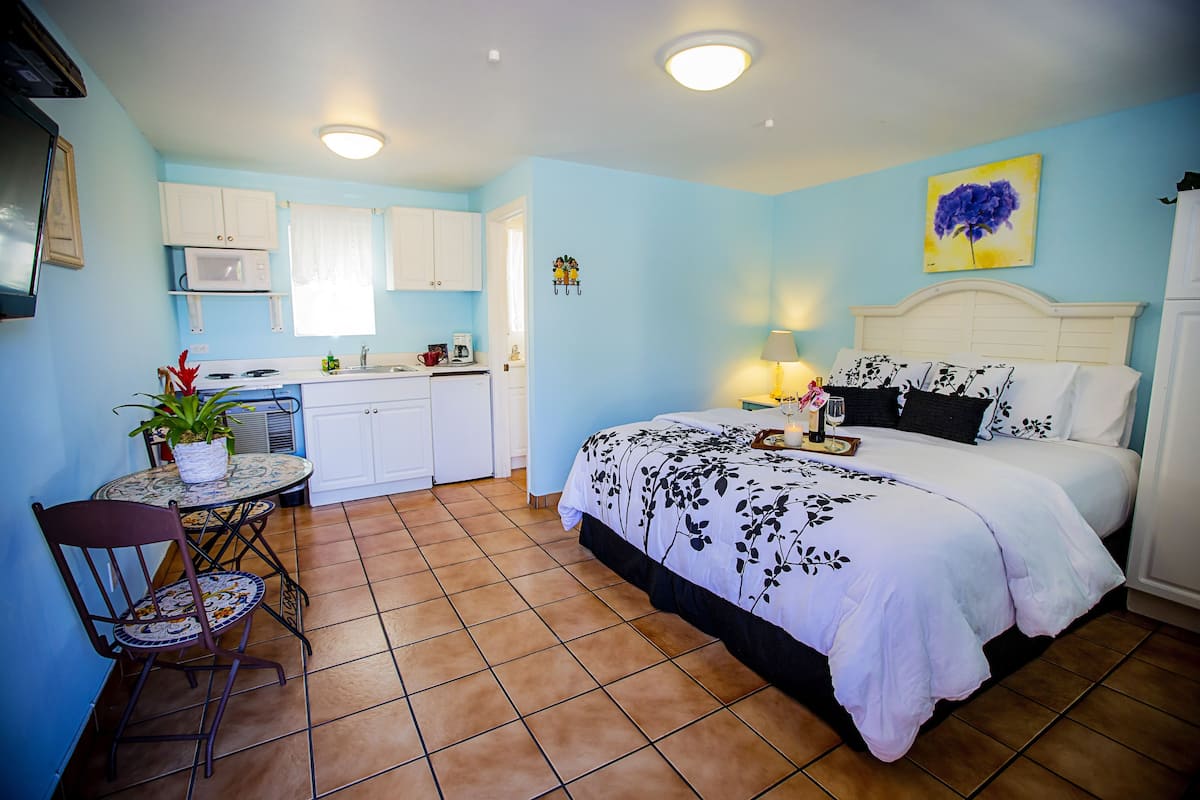 A compact hotel room with a bed, a small kitchen area, a dining table, and a chair.