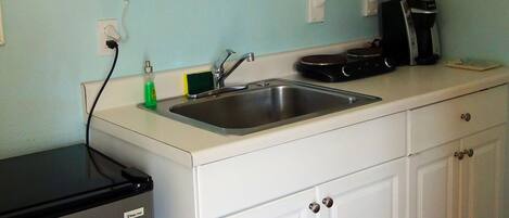 A kitchen with white cabinets, a stainless steel sink, a microwave, and a coffee maker.