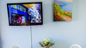 Un comedor con una mesa dispuesta para dos personas, un televisor montado en la pared y un cuadro sobre la mesa.