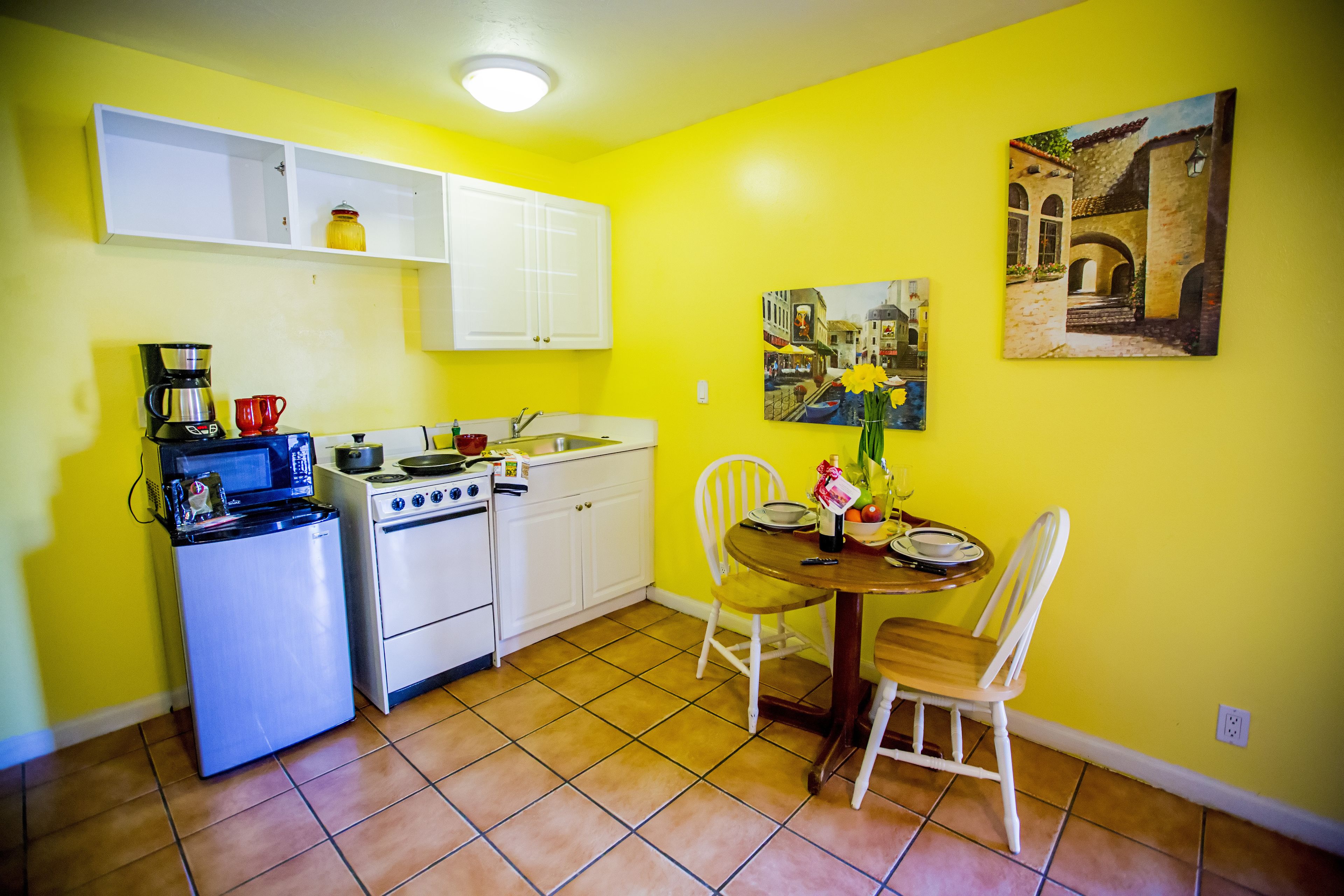 A compact kitchen with white cabinets, a small refrigerator, and a dining table with chairs.