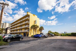 Un hotel de diverses plantes amb balcons, cotxes aparcats i palmeres.