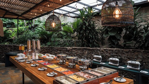Ein reichhaltiges Buffet mit verschiedenen Speisen und Besteck, umgeben von Pflanzen und Steinwänden.