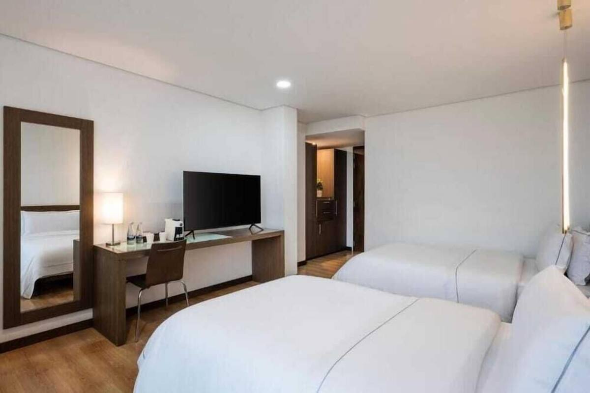 A hotel room with two beds, a desk with a TV, a chair, and a mirror.