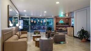 Eine moderne Lobby mit einer Couch, Sesseln und einem Couchtisch. Es gibt Topfpflanzen und ein Neonlichtschild.