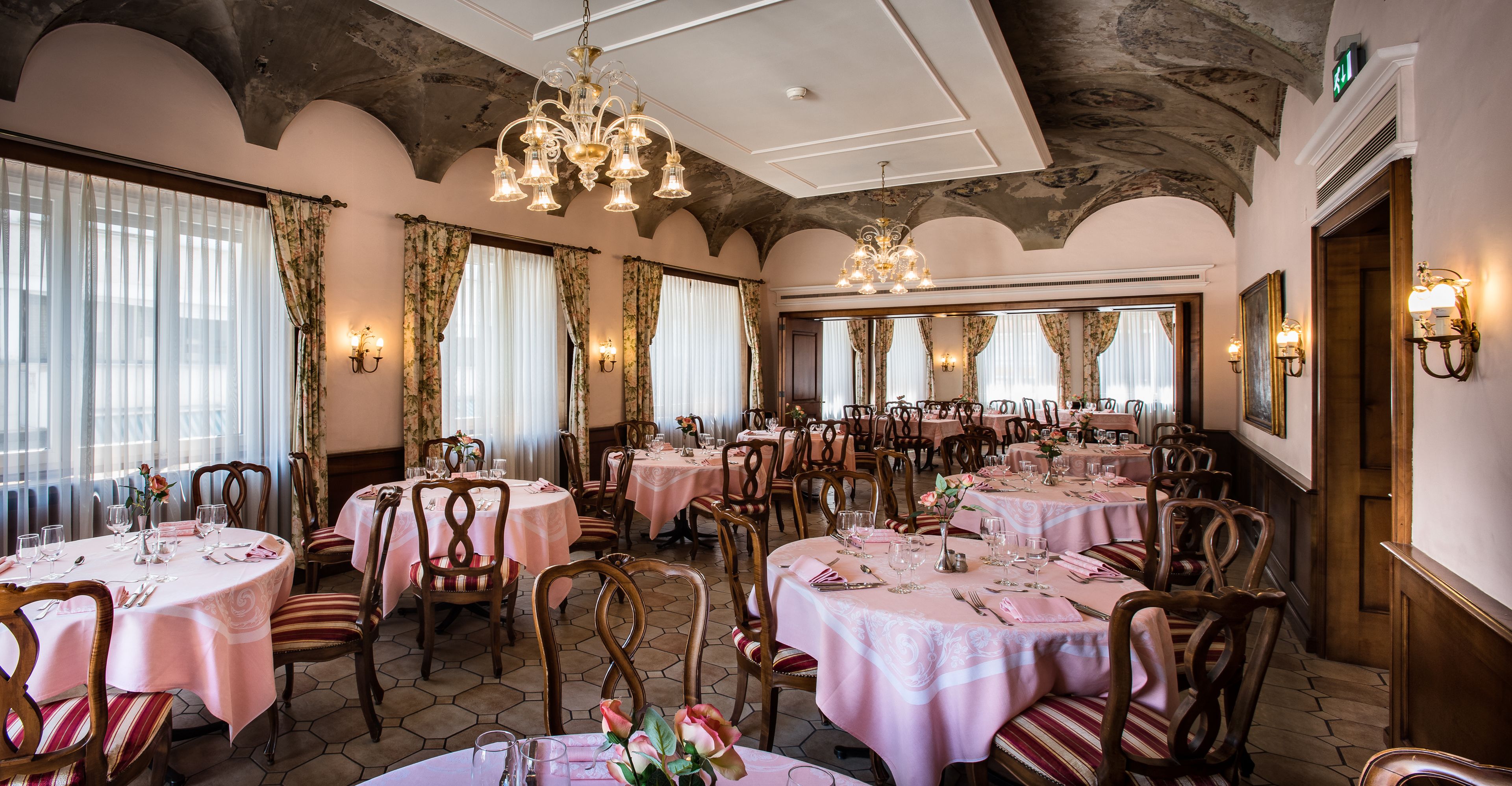 A dining area with round tables, chairs, and chandeliers.