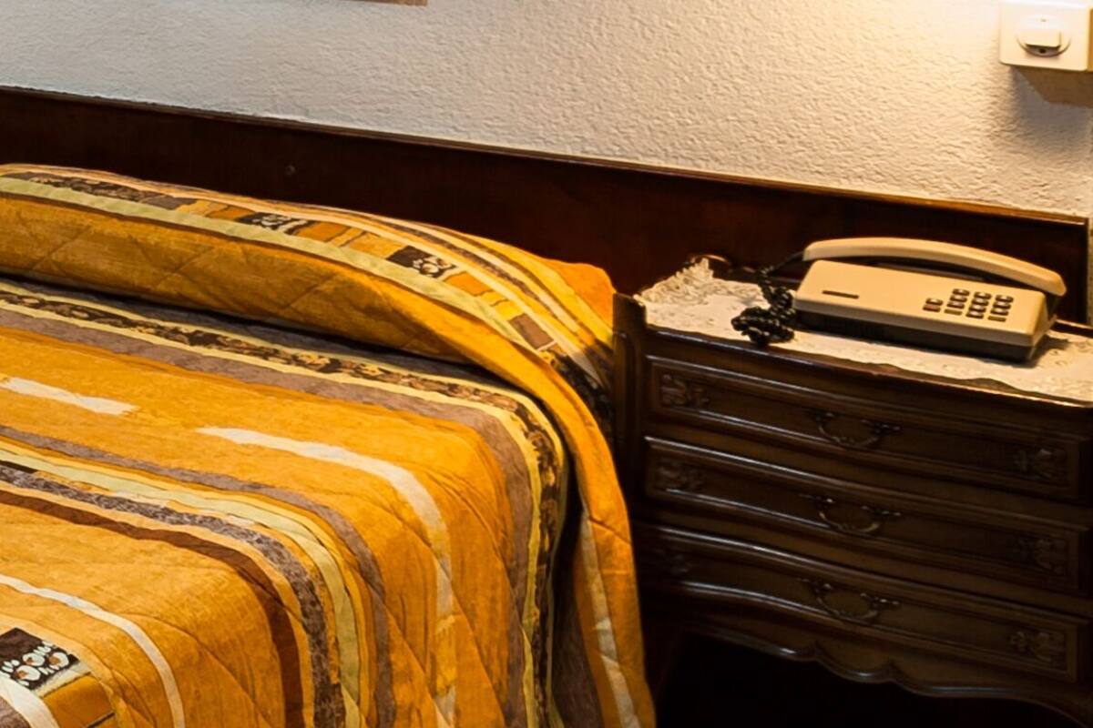A hotel room with a bed, a nightstand with a lamp, and a painting on the wall.