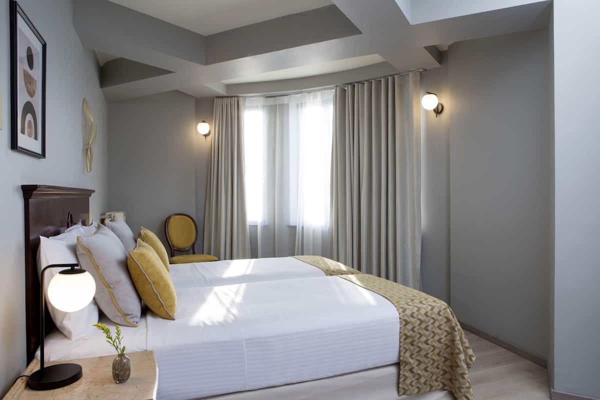 Ein modernes Hotelzimmer mit einem großen Bett, einem Nachttisch mit Lampe, einem Sessel und einem Fenster mit Vorhängen.