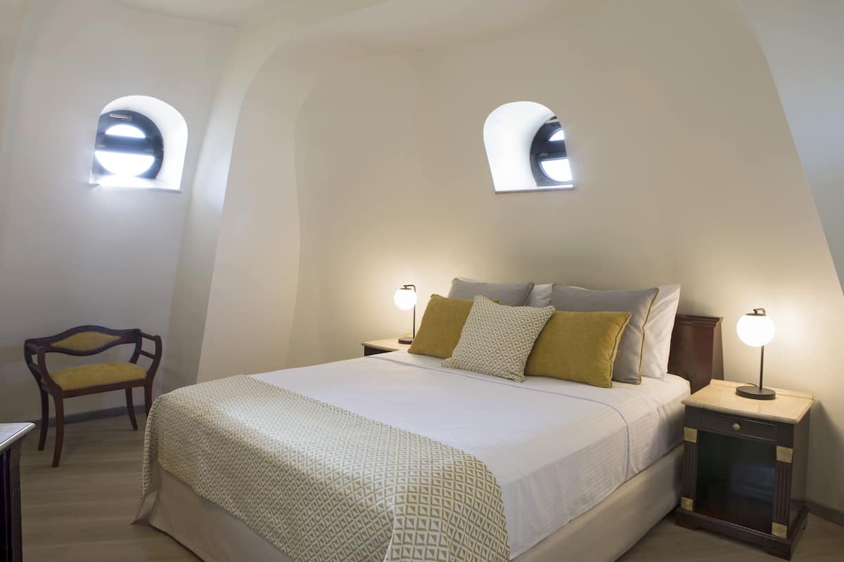 Ein Schlafzimmer mit einem großen Bett, zwei Nachttischlampen, einem Sessel und zwei Fenstern.