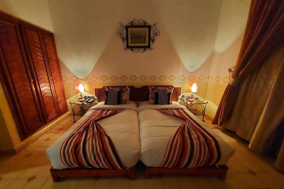 A double bed with striped bedding, two bedside tables with lamps, a wooden wardrobe, and a framed picture on the wall.