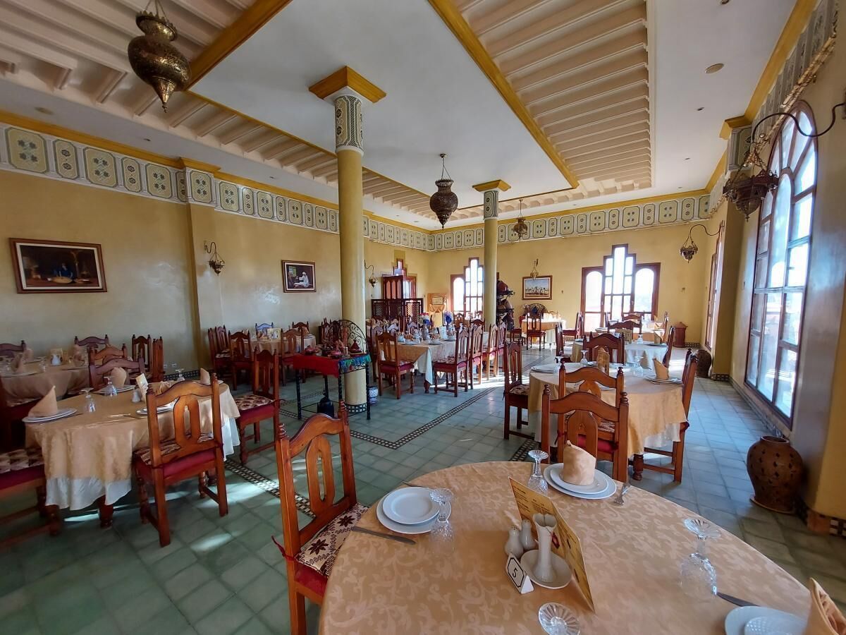 A spacious dining area with multiple tables and chairs, large windows allowing natural light, and decorative ceiling elements.