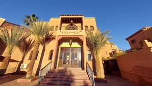 A hotel entrance with a central archway, palm trees, and a clear blue sky.