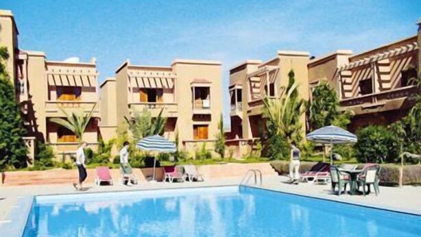 A swimming pool with lounge chairs and umbrellas, surrounded by multi-story buildings with balconies.
