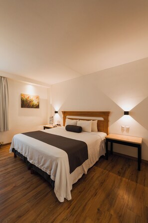 A neatly arranged bedroom with a large bed, bedside tables, and a wall-mounted painting.