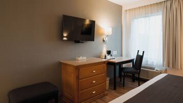 Habitación de hotel con una cama, un escritorio, una silla, un televisor y una ventana con cortinas.