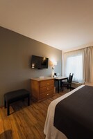Habitación de hotel con una cama, un escritorio, una silla, un televisor y una ventana con cortinas.