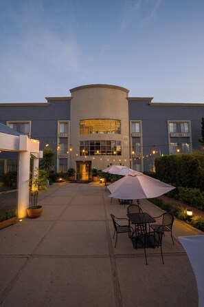 A building with a curved facade, outdoor seating area with tables and chairs, and string lights.