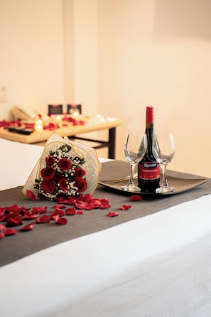 A table with a bottle of wine, two glasses, and a bouquet of red roses on a tablecloth.