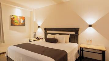 A hotel room with a large bed, bedside tables, a nightstand, a wall-mounted lamp, and a painting on the wall.
