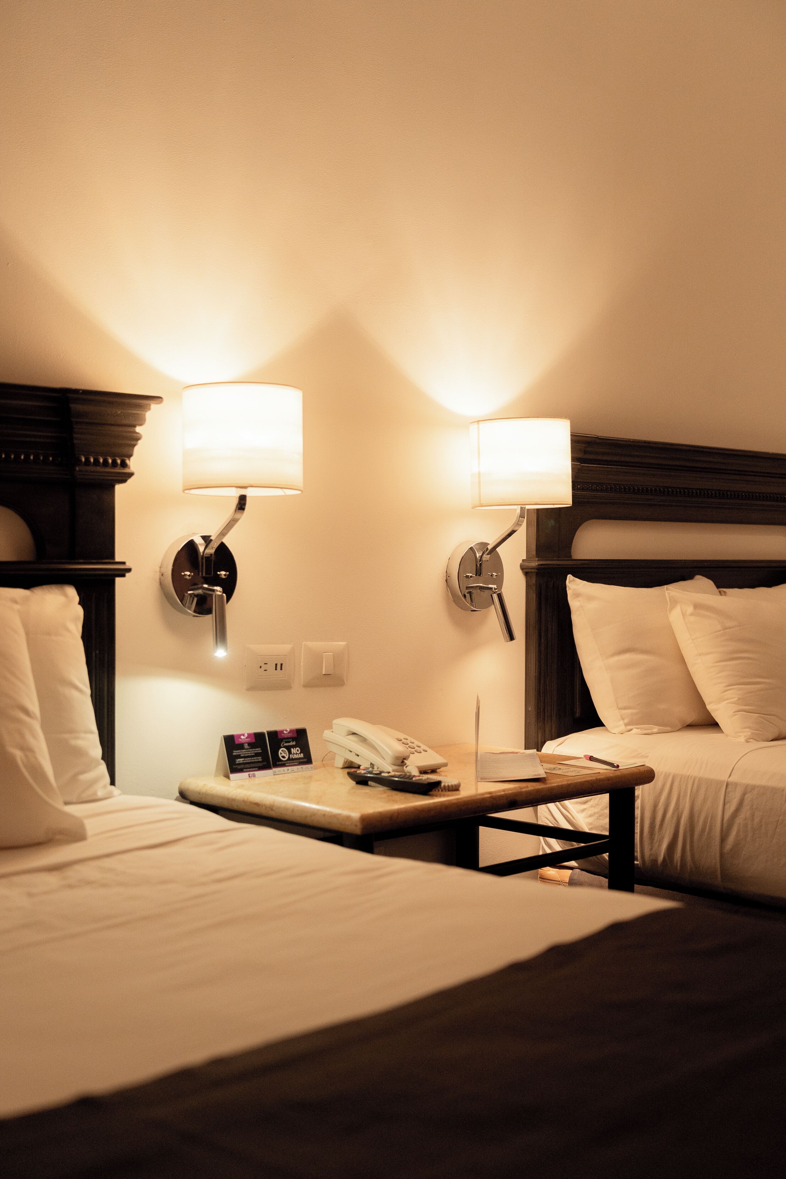 Una habitación de hotel con dos camas, una mesita de noche, una lámpara, un teléfono y una pequeña mesa.