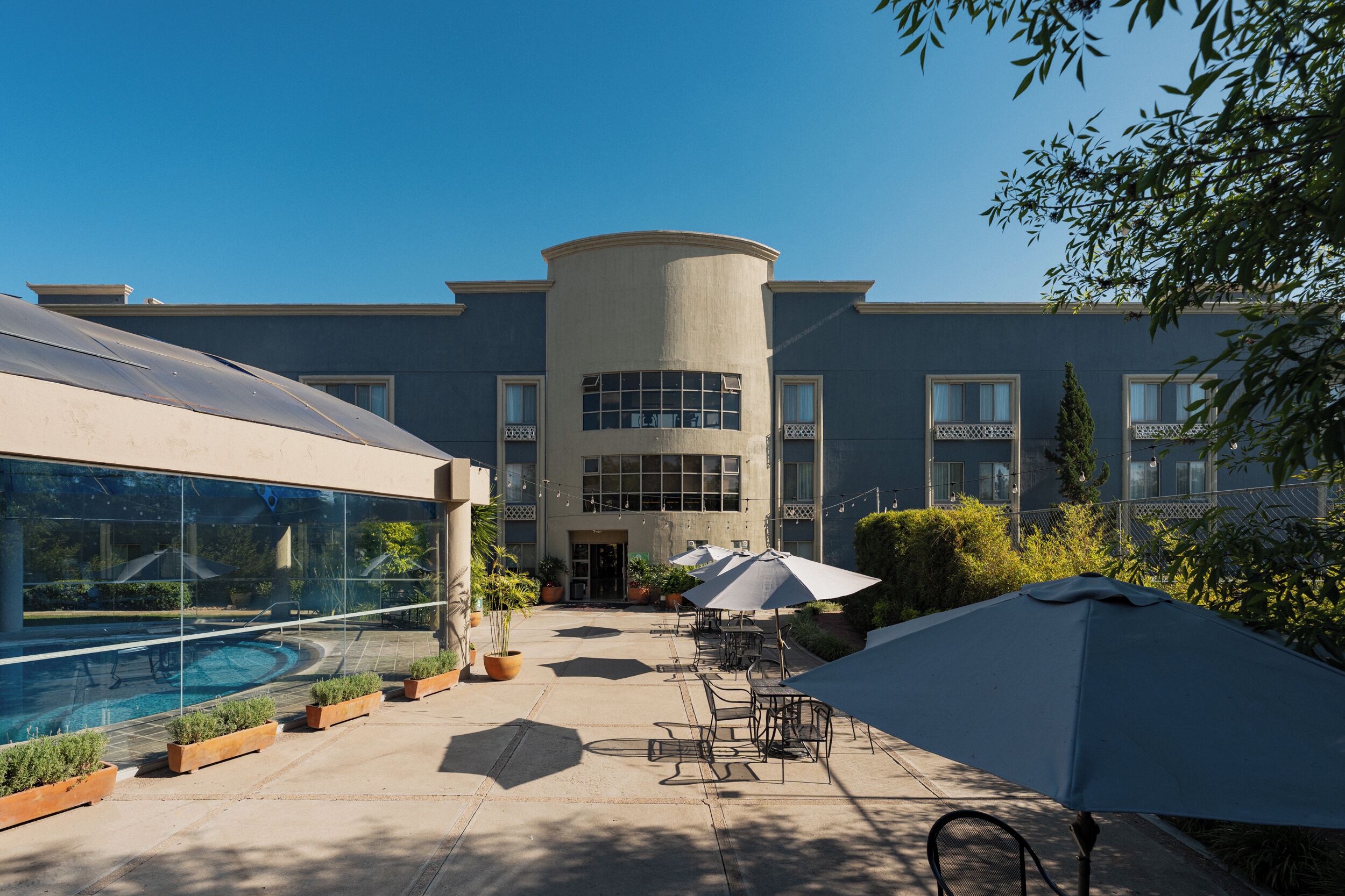 Un edificio con piscina, mobiliario exterior y plantas en macetas.