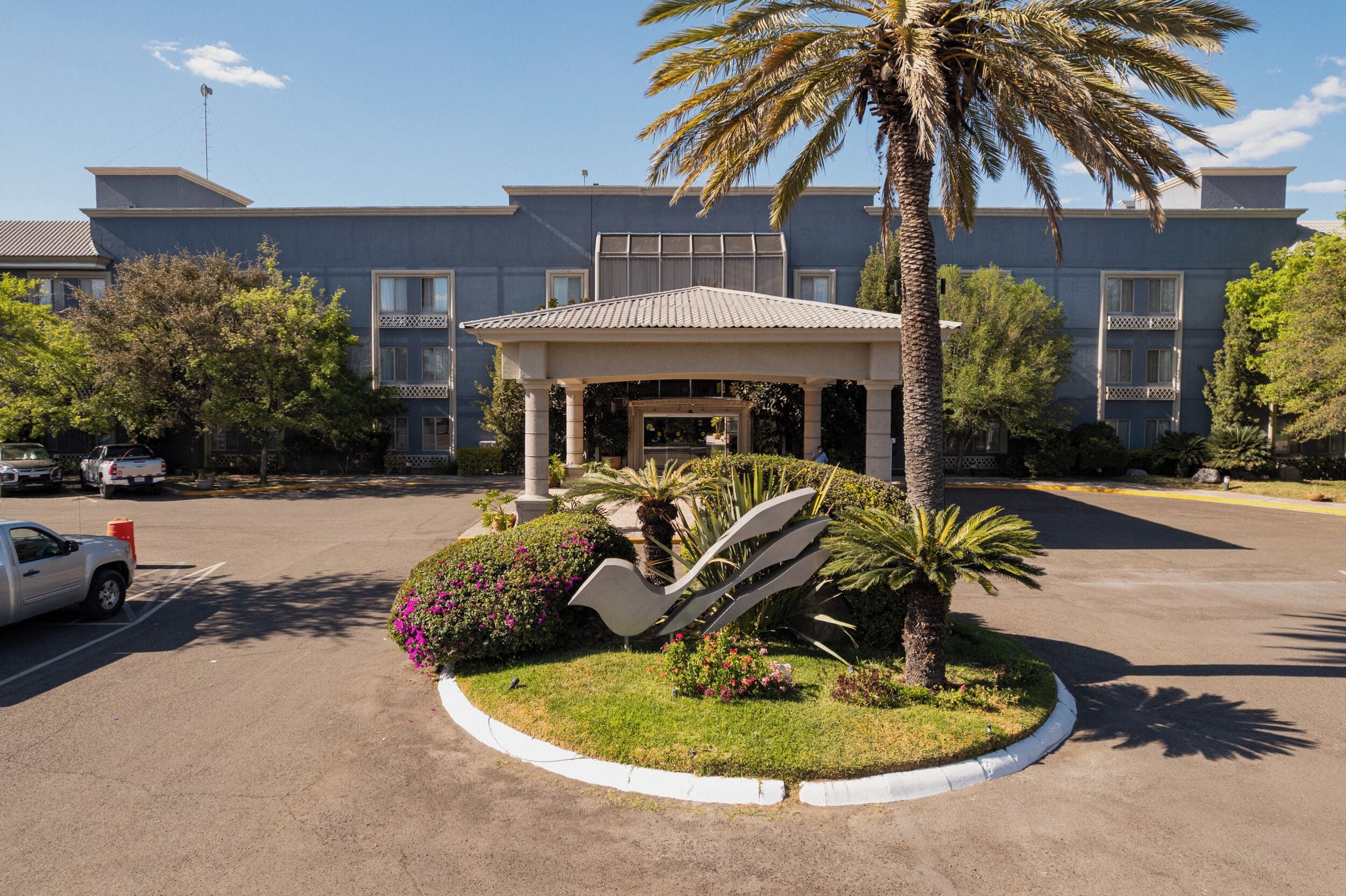 A hotel with a covered entrance, palm trees, and a parking lot.
