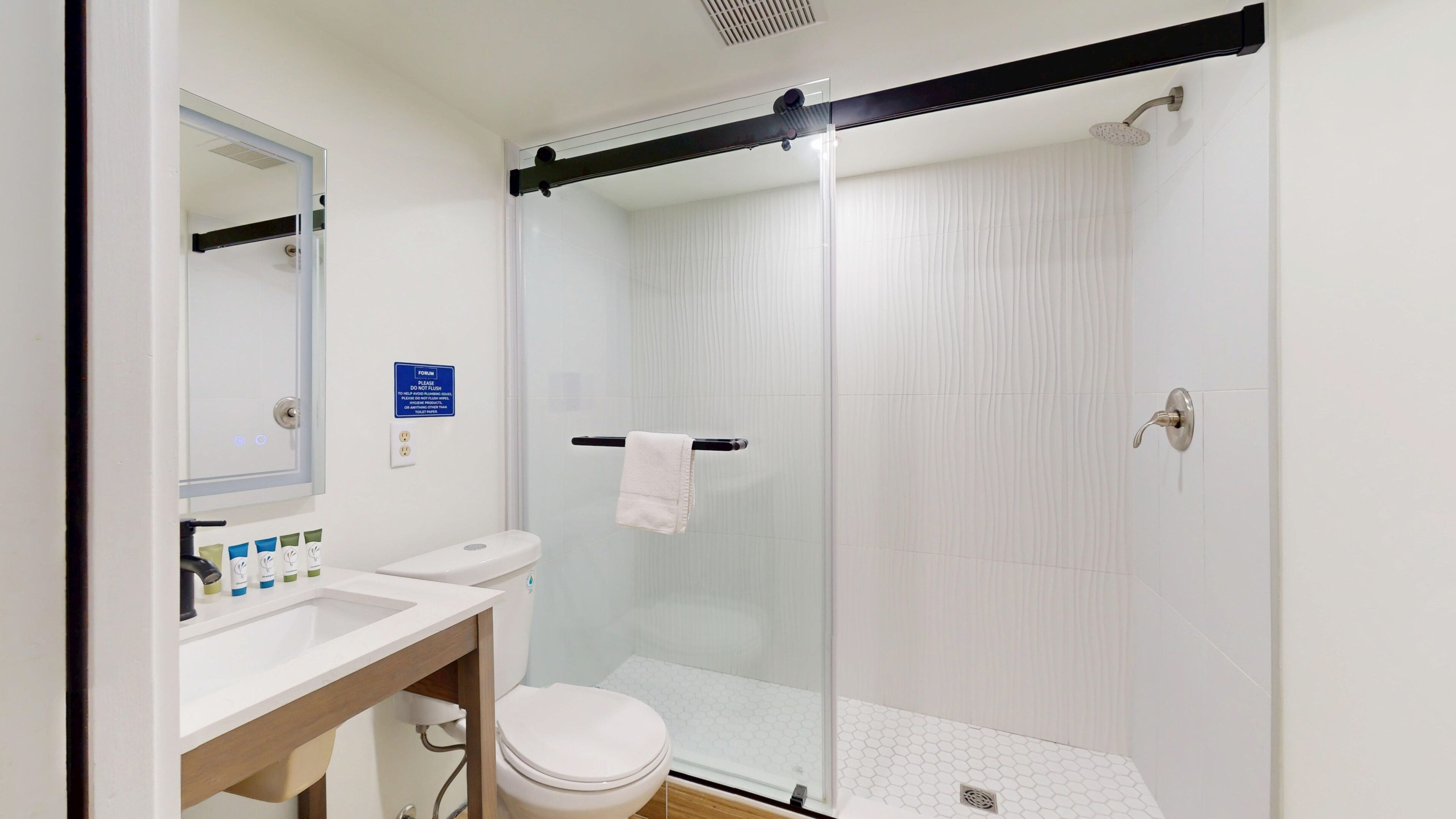 Une salle de bain moderne avec une douche en verre, des toilettes et un lavabo équipé de produits de toilette.