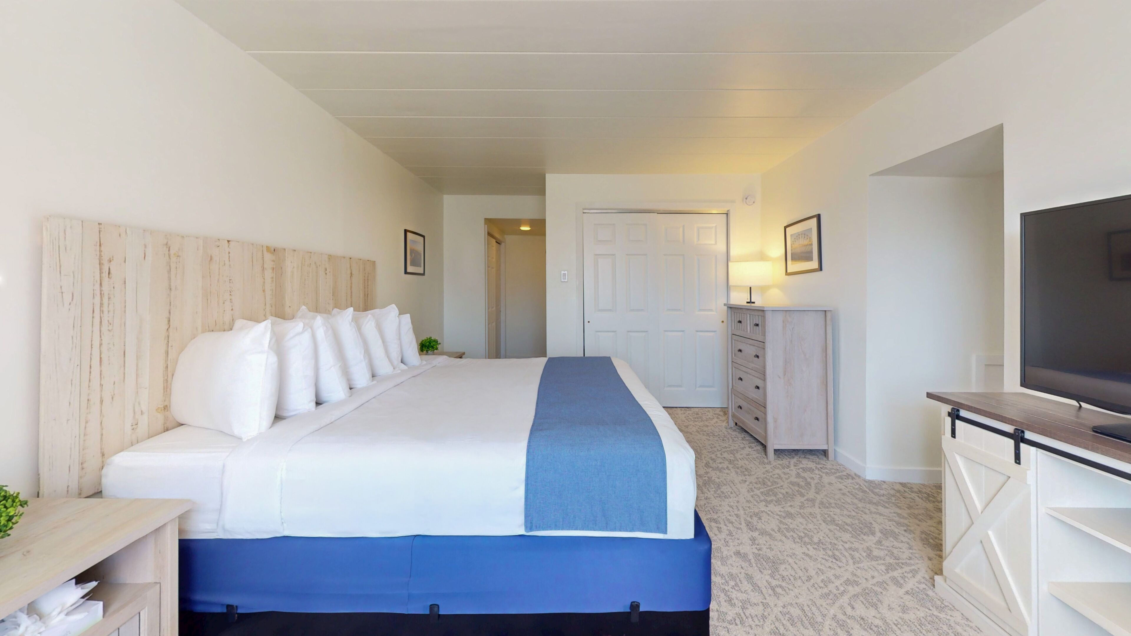 Una habitación de hotel con una cama, televisión, cómoda y una puerta.