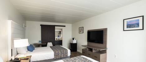 Quarto de hotel com duas camas, televisão, secretária com luminária, mesa pequena e um quadro na parede.