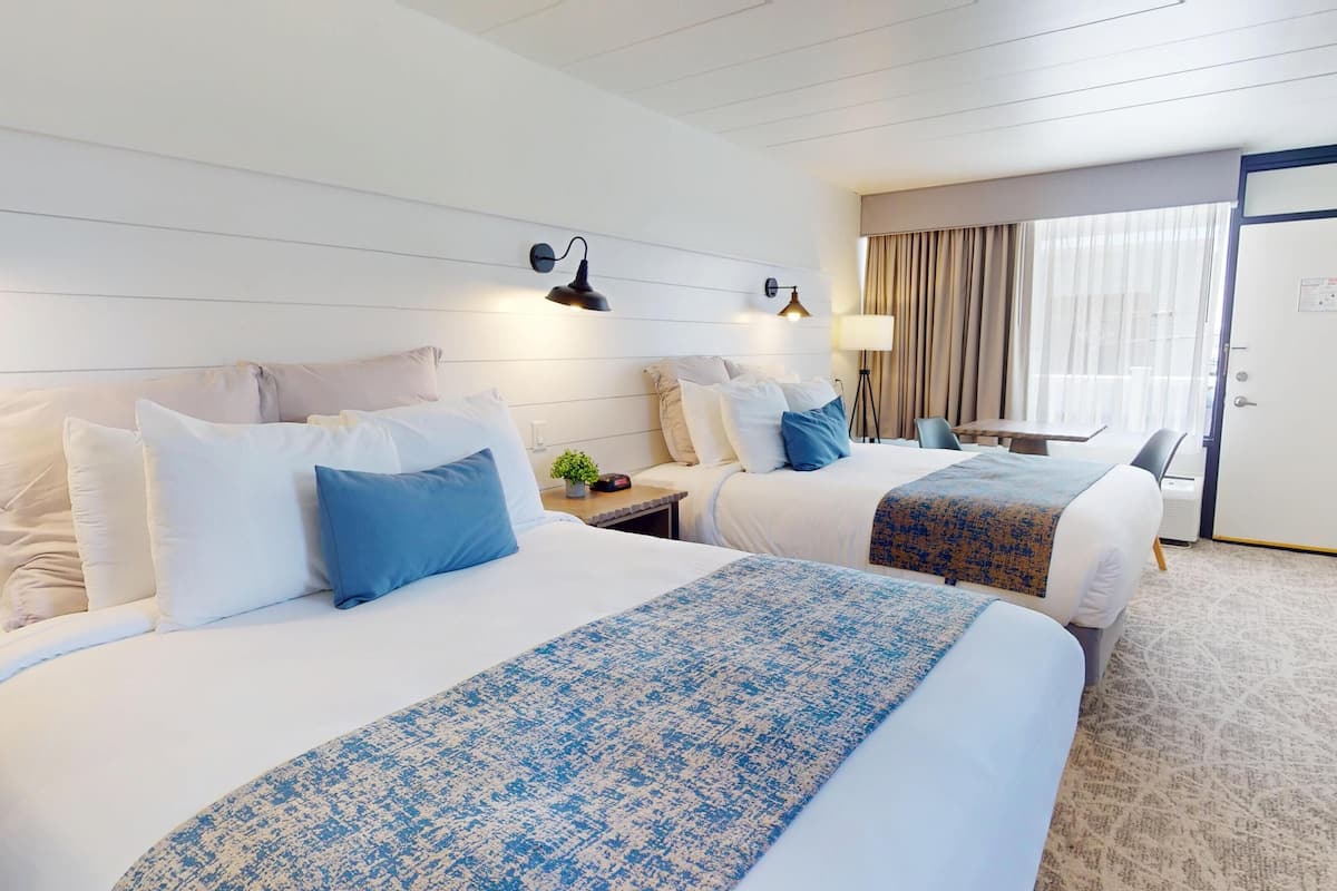 A hotel room with two beds, a desk, a chair, a lamp, and a door.