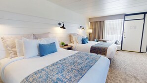 A hotel room with two beds, a desk, a chair, a lamp, and a door. - The Forum (Ocean City)