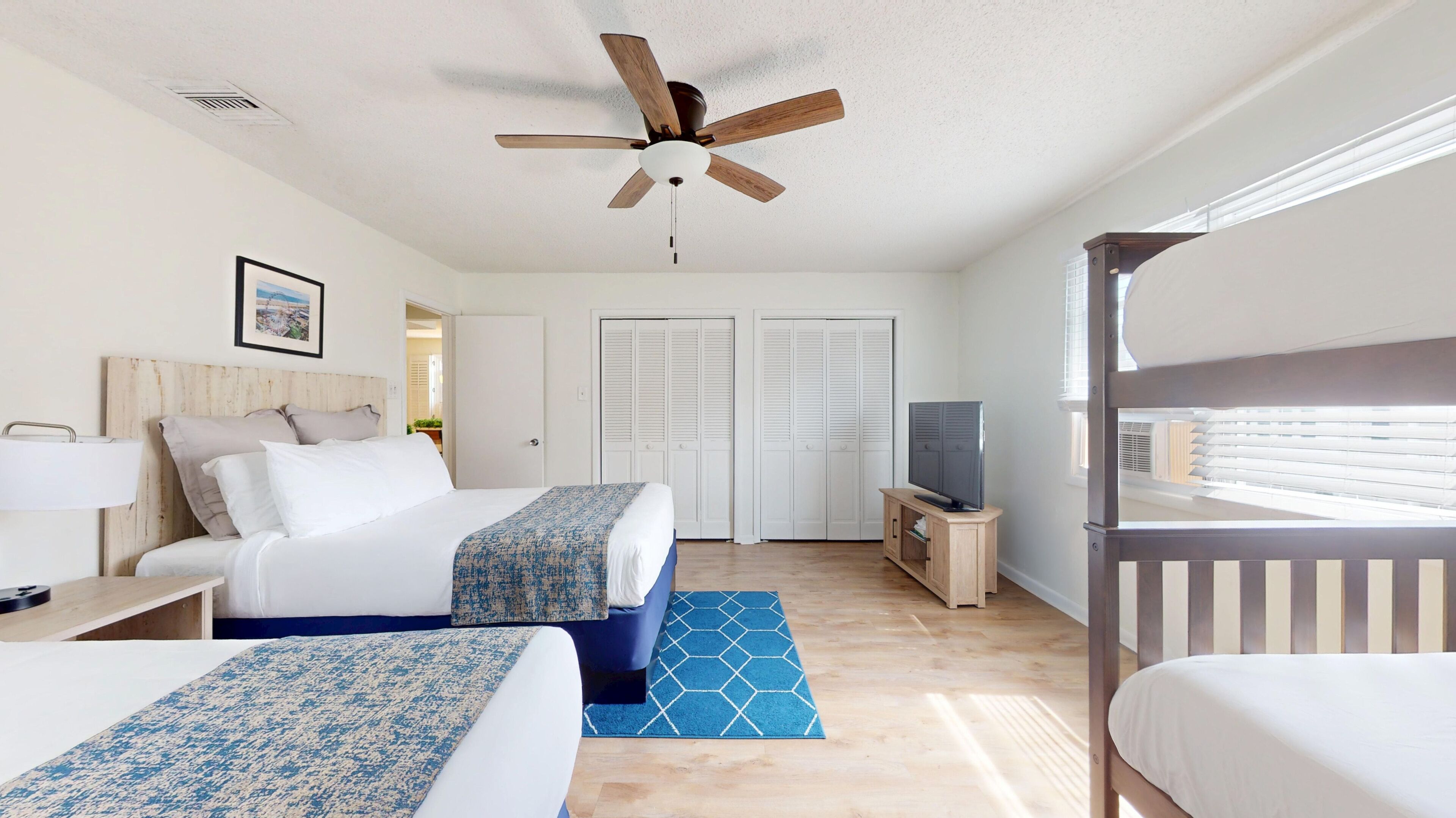 A hotel room with two beds, a ceiling fan, a TV, and a window with blinds.