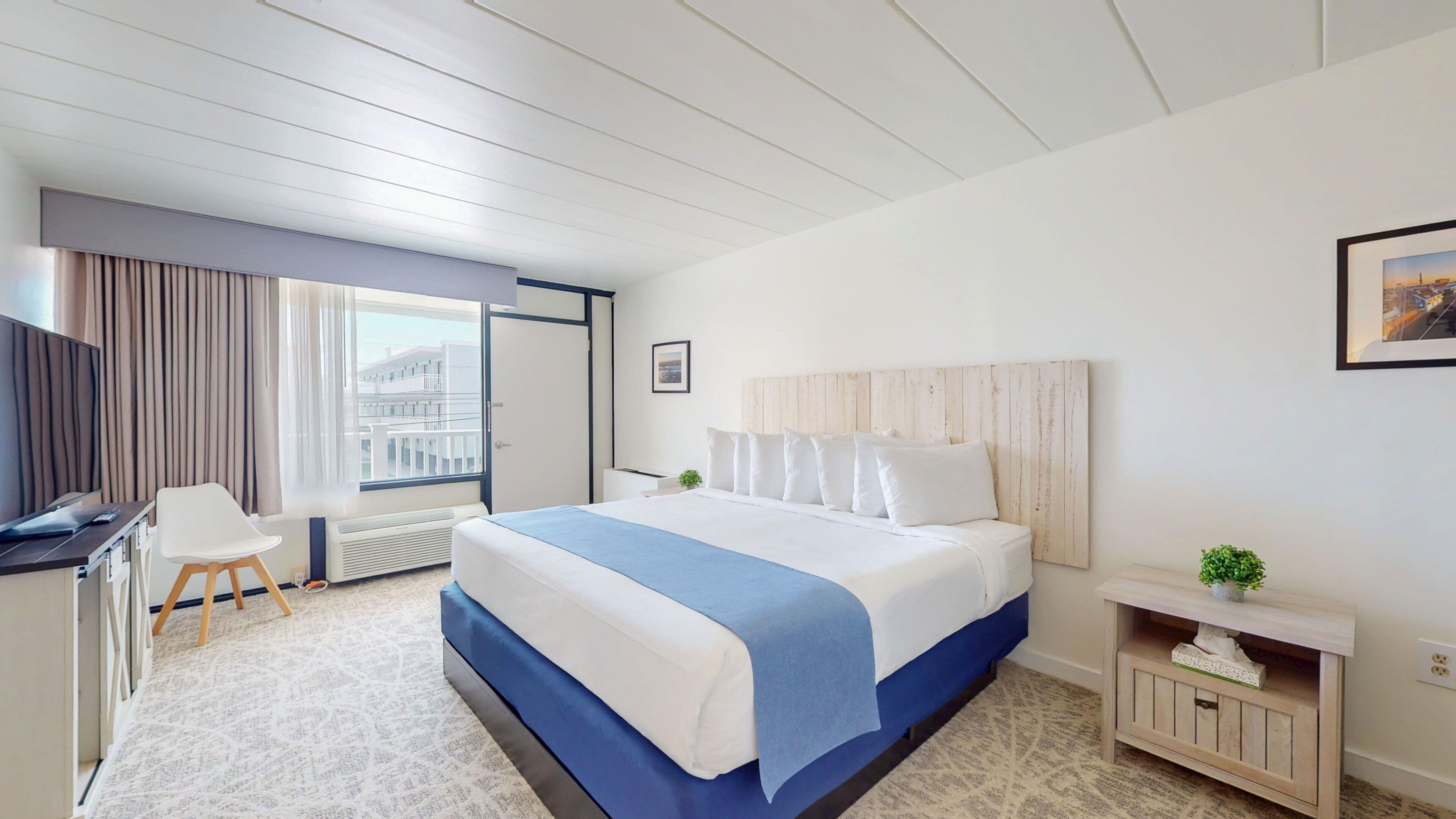 Ein Hotelzimmer mit einem Bett, einem Schreibtisch, einem Stuhl, einer kleinen Pflanze und einem Fenster mit Vorhängen.