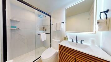 Een moderne badkamer met een douche met glazen wand, een toilet, een wastafel met spiegel en een handdoekhouder.