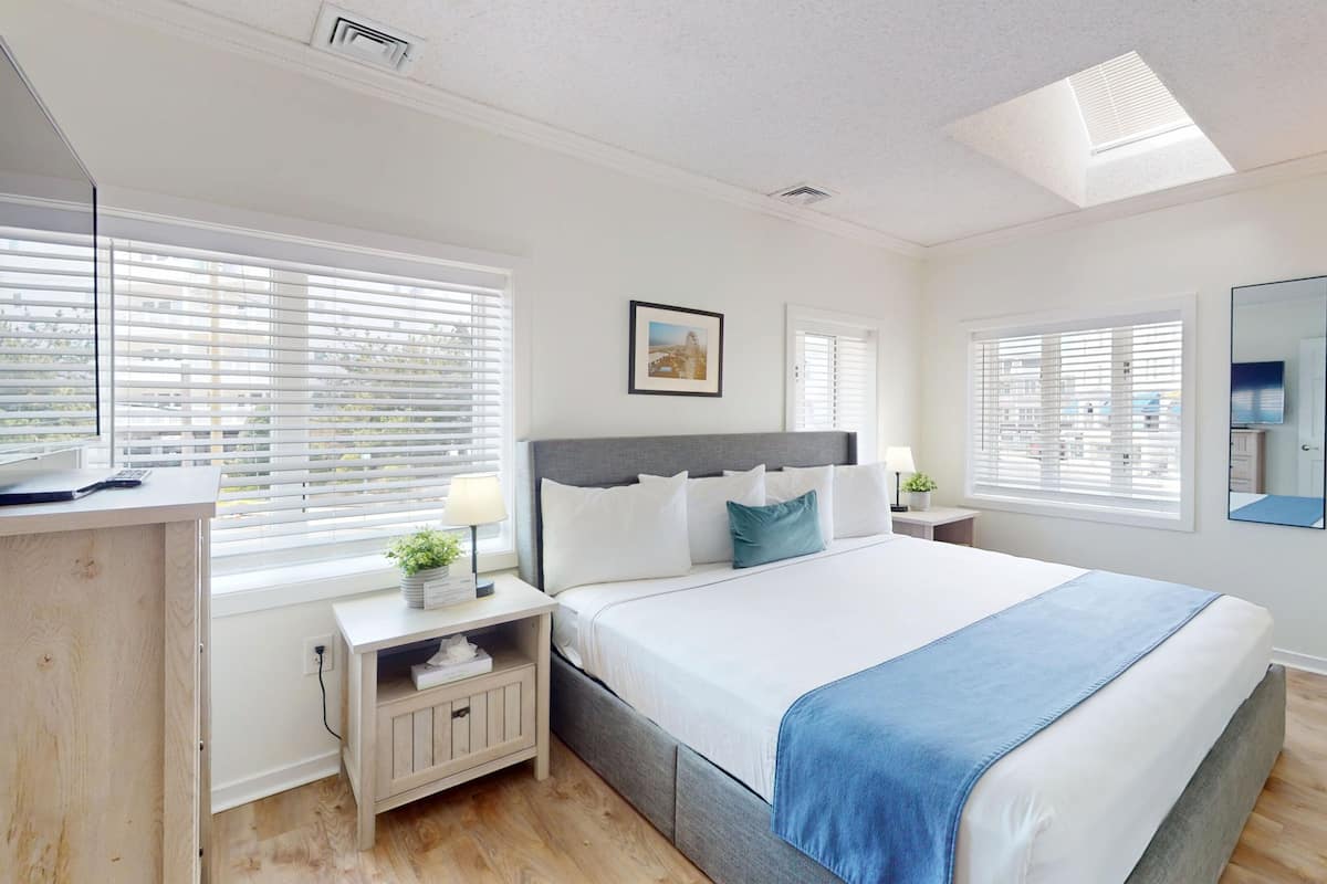 A bedroom with a bed, bedside tables, a desk, a mirror, and a skylight.