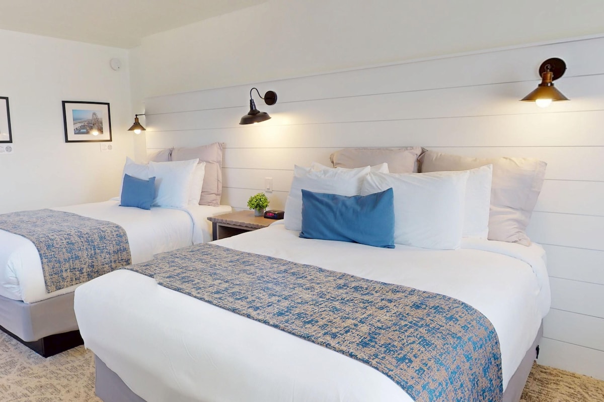 A hotel room with two beds, a nightstand, and two wall-mounted lamps.