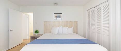 Ein Schlafzimmer mit Bett, Nachttisch, Topfpflanze und Kleiderschrank.