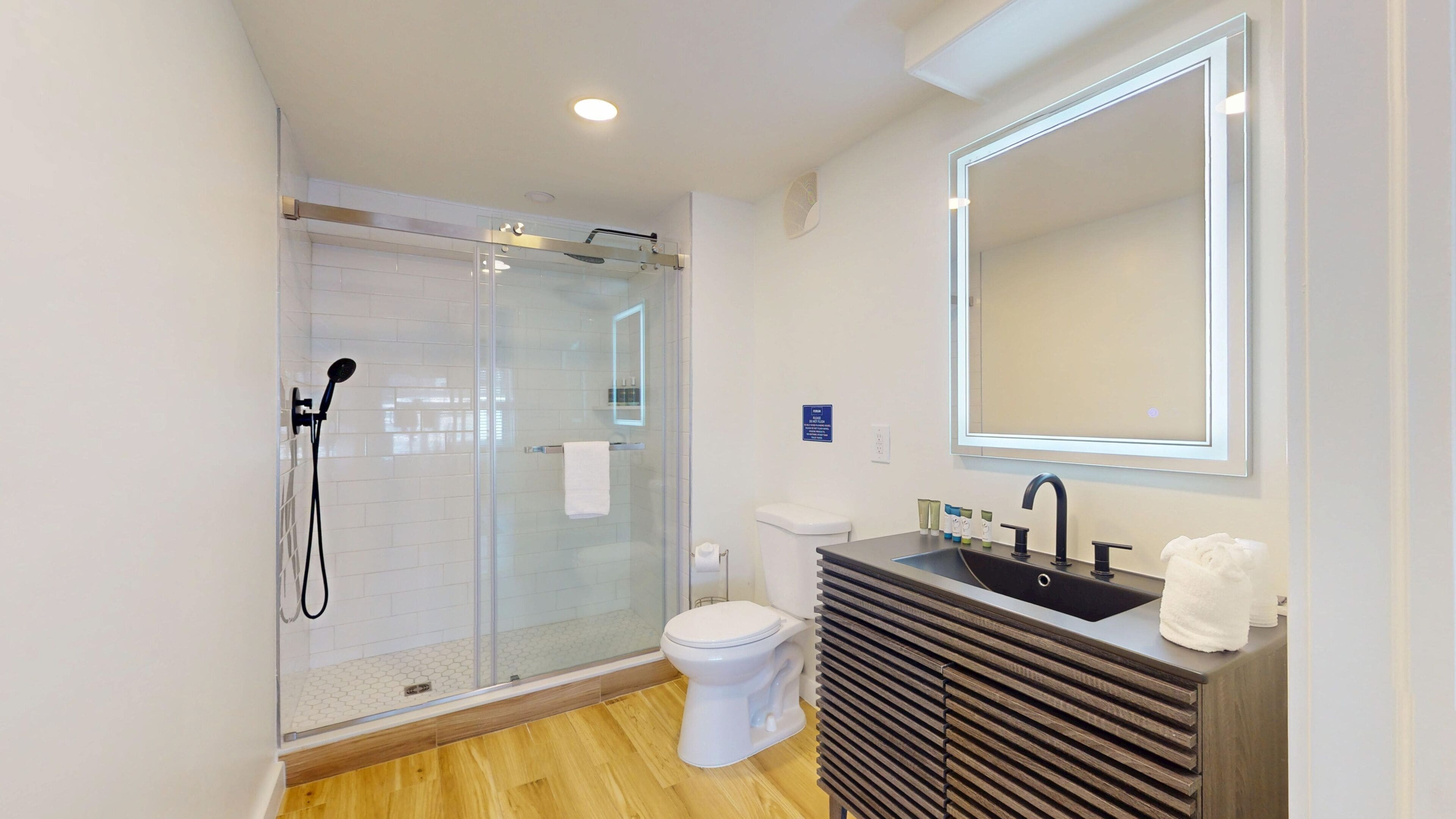 A modern bathroom with a glass shower enclosure, a toilet, a sink with a mirror, and wooden vanity.