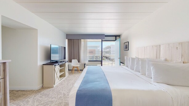 Habitación de hotel con cama, televisión en un escritorio, una silla y balcón con vistas.
