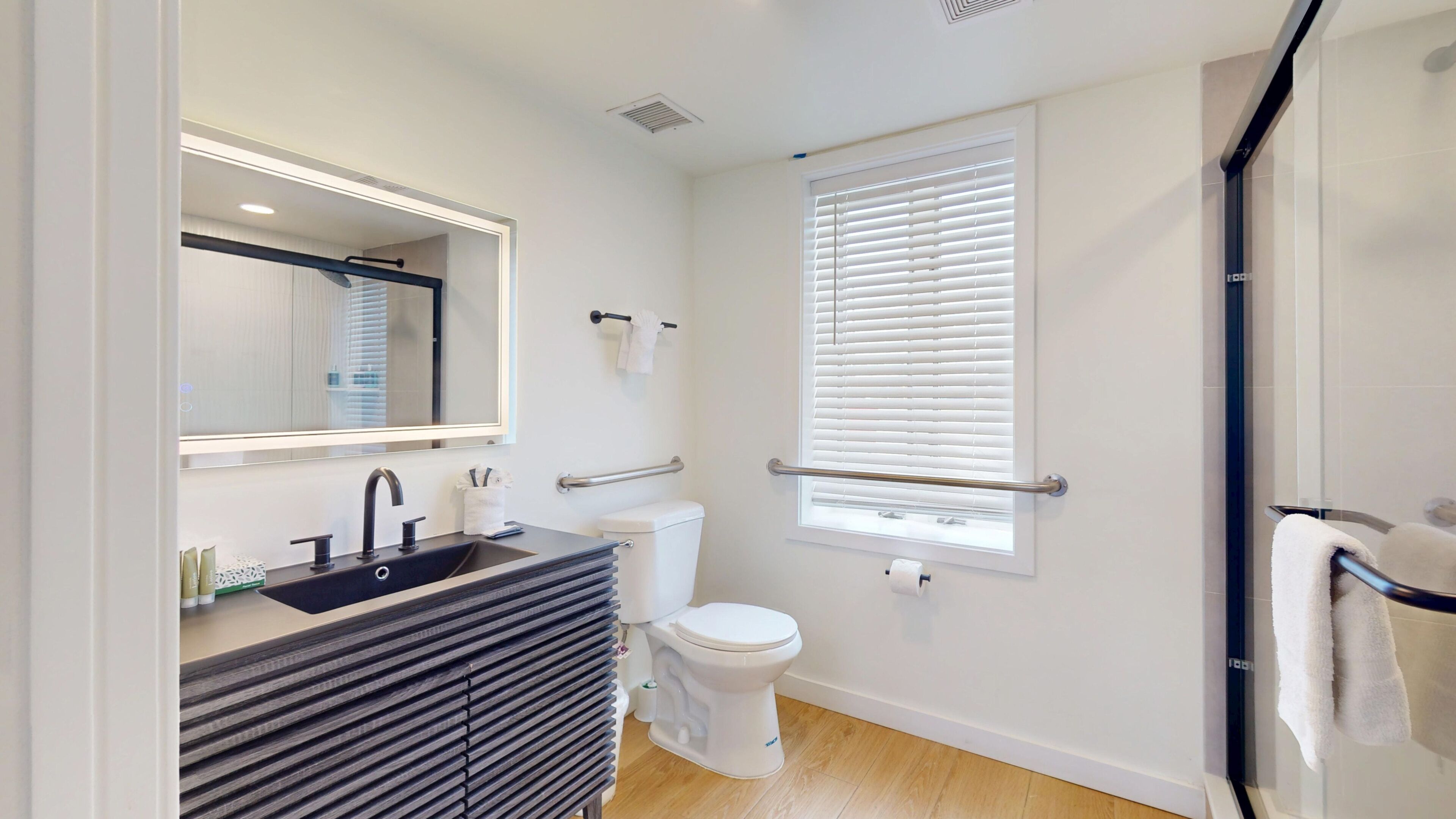 A modern bathroom with a sink, toilet, and window with blinds.