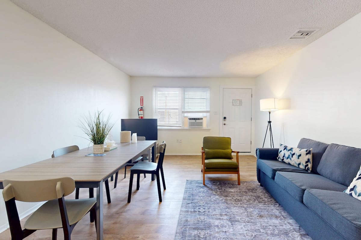 A modern living room with a dining area, a sofa, a lamp, and a chair.