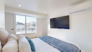 Un dormitorio con cama, televisor montado en la pared y balcón con vistas a edificios.