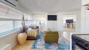 Una sala de estar moderna con un sofá, un sillón verde, un jarrón grande y un televisor de pantalla plana.