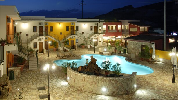 Un hotel con piscina, mobiliario exterior y montañas al fondo.